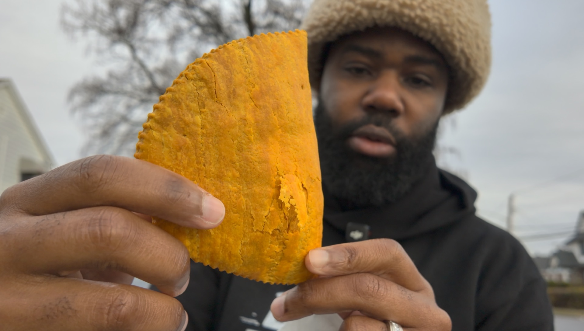 Winston inspecting a whole golden Jamaican beef patty up close